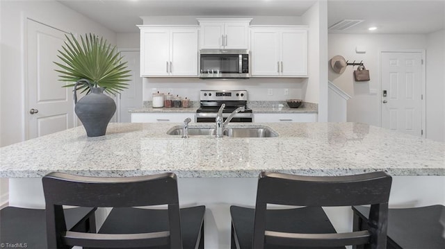 2124 Monk Dr, Haw River, NC 27258 - kitchen with stainless steel appliances, a sink, white cabinetry, a kitchen bar, and recessed lighting