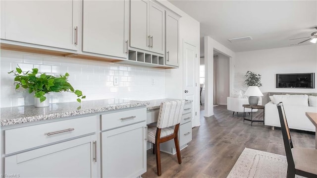 kitchen with a ceiling fan, light stone counters, backsplash, open floor plan, and wood finished floors