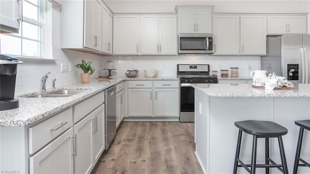 kitchen with backsplash, a kitchen bar, appliances with stainless steel finishes, wood finished floors, and a sink