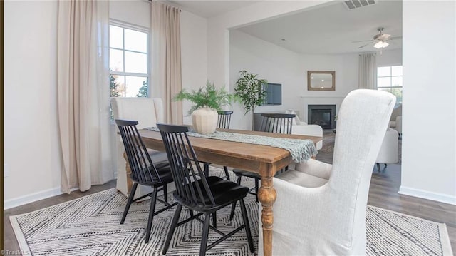 dining area with a glass covered fireplace, ceiling fan, baseboards, and wood finished floors