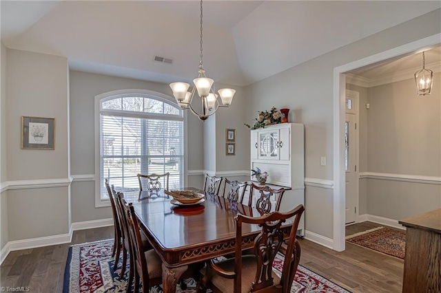 dining space featuring dark wood-type flooring, vaulted ceiling, and a notable chandelier