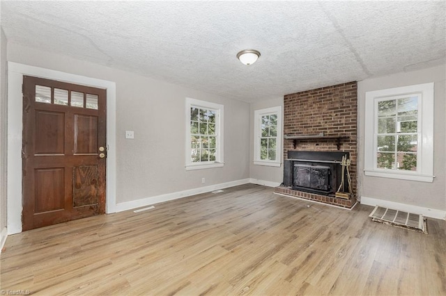 unfurnished living room featuring light hardwood / wood-style floors, a wealth of natural light, brick wall, and a brick fireplace