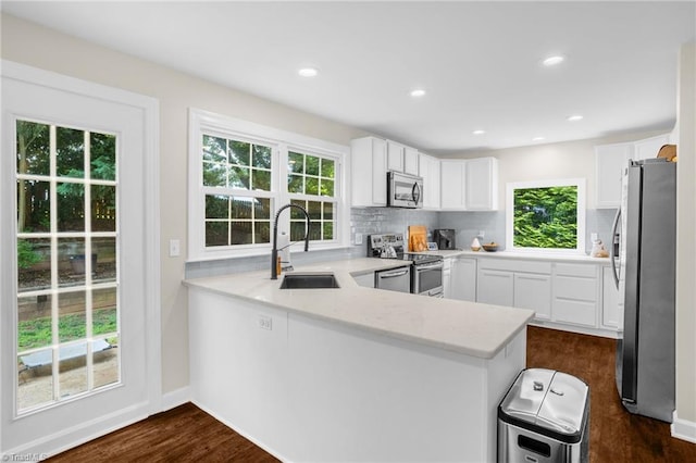 kitchen with stainless steel appliances, a sink, a peninsula, decorative backsplash, and dark wood-style floors