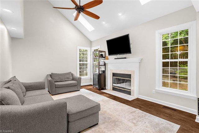 living room with ceiling fan, a skylight, high vaulted ceiling, a high end fireplace, and wood finished floors