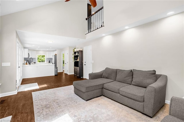 living area featuring a ceiling fan, baseboards, dark wood-style flooring, a towering ceiling, and recessed lighting