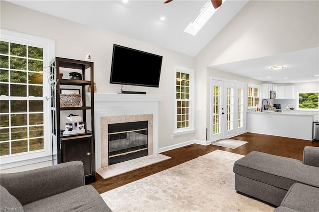 living room featuring a ceiling fan, a skylight, dark wood-style floors, a fireplace, and high vaulted ceiling