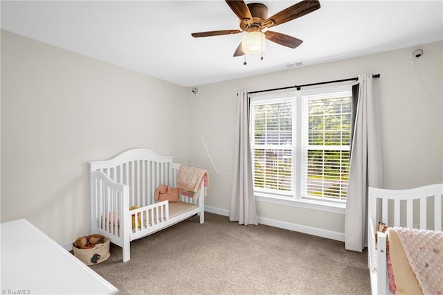 bedroom with carpet flooring, baseboards, a crib, and a ceiling fan