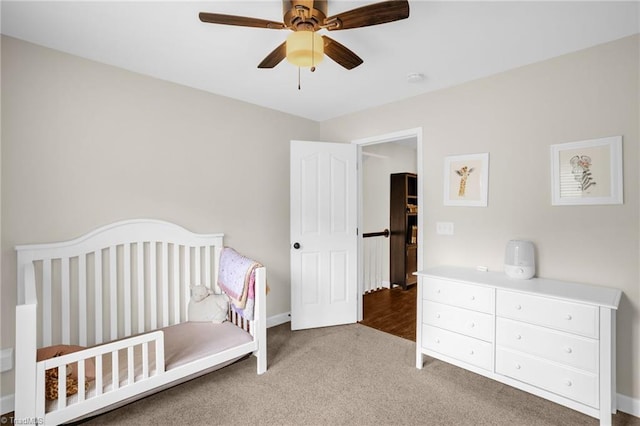 bedroom with carpet floors, a nursery area, baseboards, and a ceiling fan