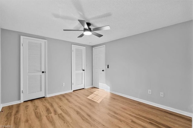 unfurnished bedroom with multiple closets, light wood-style flooring, a textured ceiling, baseboards, and ceiling fan