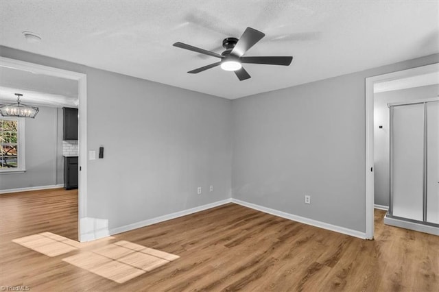 empty room with baseboards, a textured ceiling, wood finished floors, and ceiling fan with notable chandelier