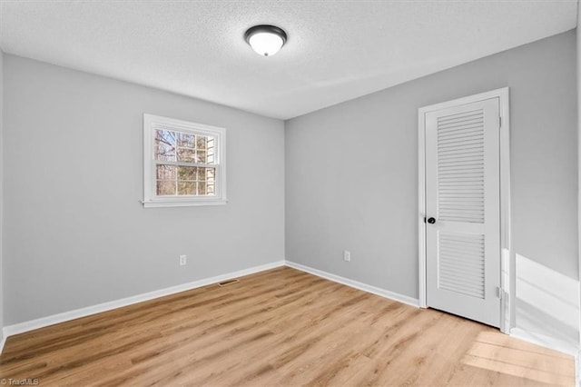 unfurnished bedroom featuring light wood finished floors, a closet, a textured ceiling, and baseboards