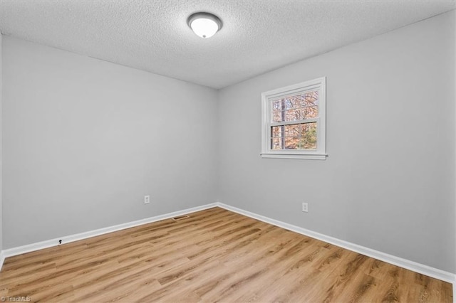 empty room with baseboards, a textured ceiling, and light wood finished floors