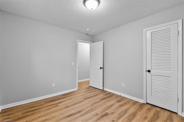 unfurnished bedroom featuring light wood-style flooring, baseboards, a closet, and a textured ceiling