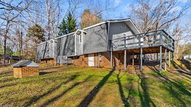 exterior space featuring a gambrel roof, a deck, a yard, roof with shingles, and brick siding