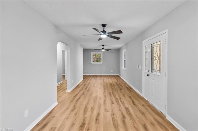 unfurnished living room featuring light wood-type flooring, a ceiling fan, a textured ceiling, arched walkways, and baseboards