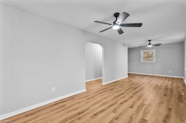 empty room featuring baseboards, arched walkways, light wood-style floors, and a textured ceiling