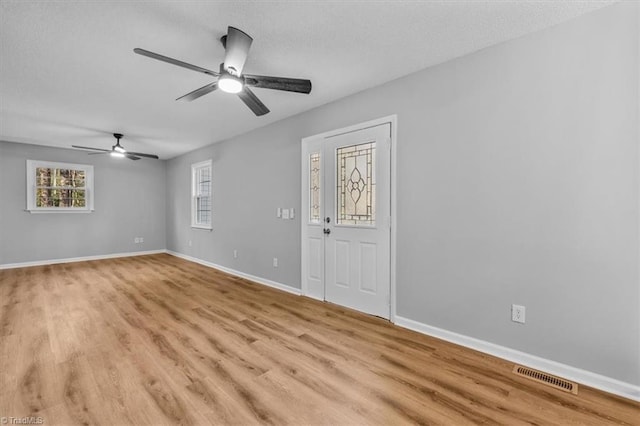 spare room featuring visible vents, a ceiling fan, a textured ceiling, light wood-style floors, and baseboards