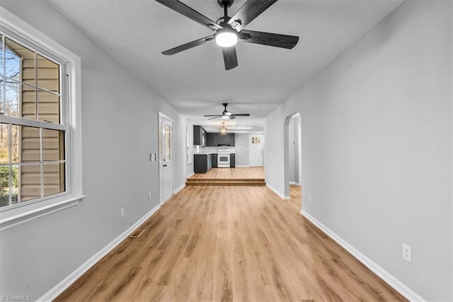 unfurnished living room with a ceiling fan, baseboards, light wood-style flooring, arched walkways, and a textured ceiling