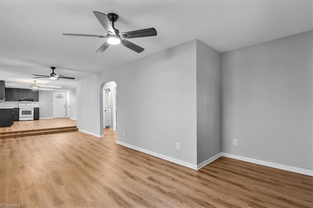 unfurnished living room featuring ceiling fan, light wood-style floors, arched walkways, and baseboards