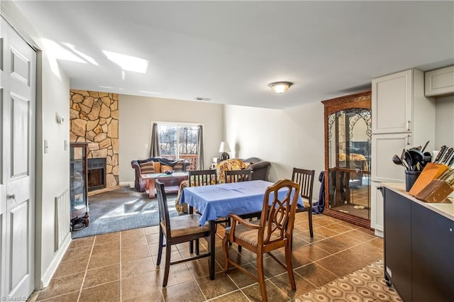 dining room featuring a stone fireplace and dark tile patterned floors