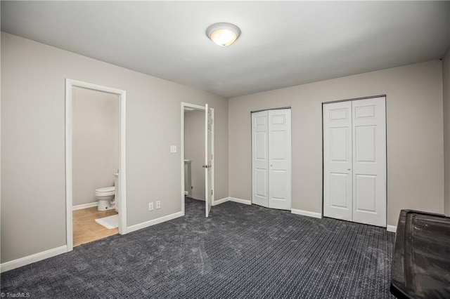 unfurnished bedroom featuring dark colored carpet, two closets, and connected bathroom