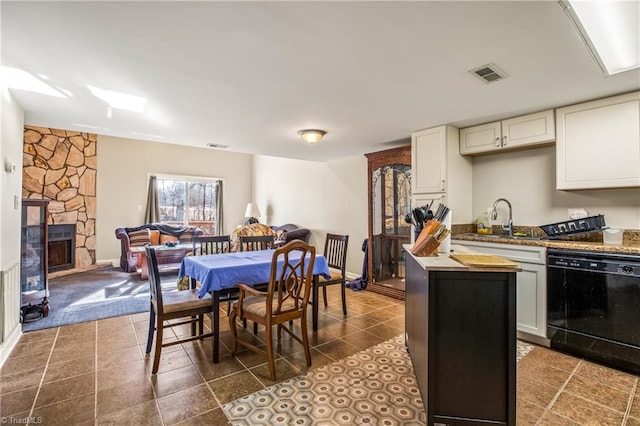 kitchen featuring a stone fireplace, white cabinetry, dishwasher, sink, and dark tile patterned flooring