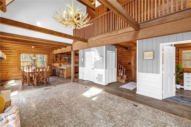 unfurnished living room featuring stairway, wood finished floors, an inviting chandelier, a high ceiling, and beam ceiling