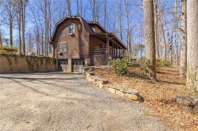 view of property exterior featuring a garage, a gambrel roof, gravel driveway, and log exterior