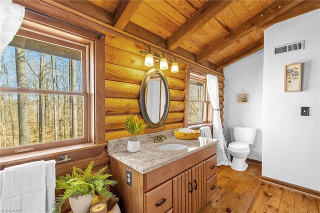 half bath with visible vents, baseboards, beamed ceiling, toilet, and wood-type flooring