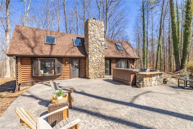 view of front of home featuring area for grilling, a patio, roof with shingles, log exterior, and a chimney