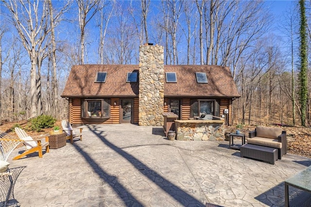 exterior space with log siding, roof with shingles, a chimney, and a patio area