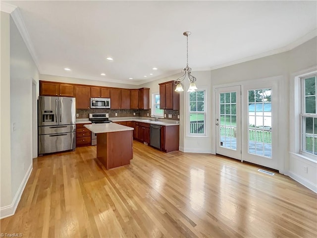 kitchen with pendant lighting, stainless steel appliances, light wood-type flooring, and a center island