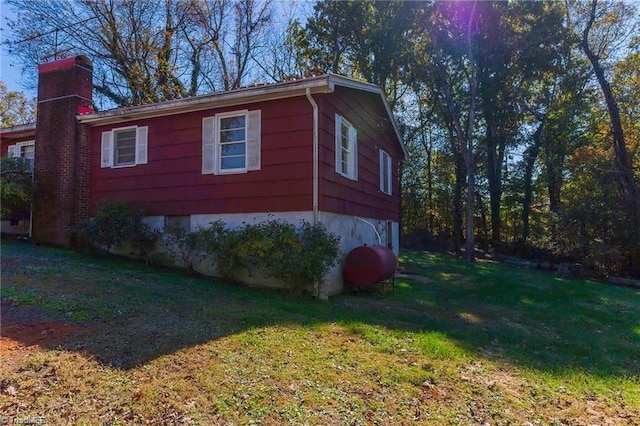 view of side of property with a yard, a chimney, and heating fuel