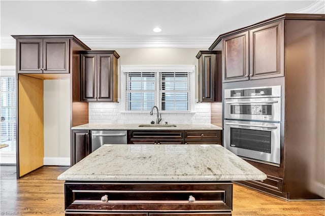 kitchen with sink, light hardwood / wood-style flooring, dark brown cabinets, a kitchen island, and appliances with stainless steel finishes