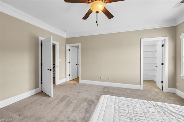 unfurnished bedroom featuring ceiling fan, a spacious closet, ornamental molding, and light carpet