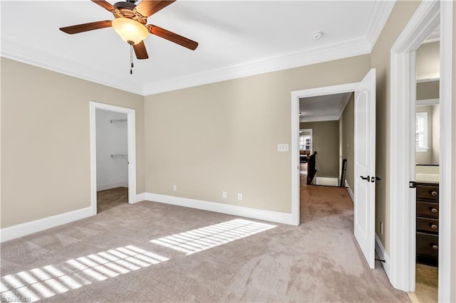 unfurnished bedroom with a walk in closet, light colored carpet, ceiling fan, and ornamental molding