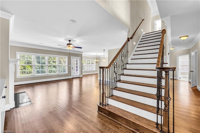 stairway featuring wood-type flooring, ceiling fan with notable chandelier, and crown molding