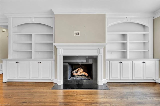 unfurnished living room featuring built in shelves, hardwood / wood-style floors, and ornamental molding