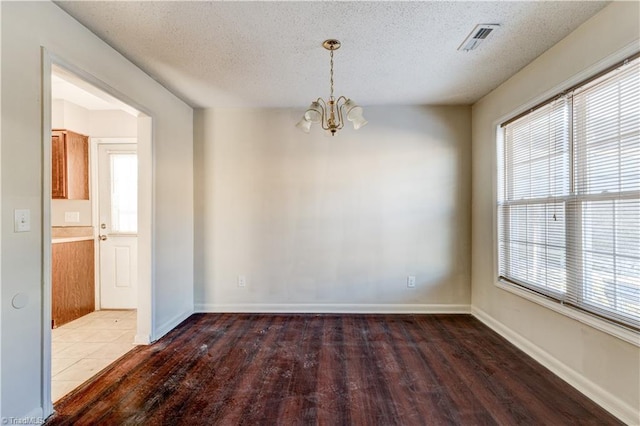 empty room with a wealth of natural light, dark hardwood / wood-style floors, a textured ceiling, and a chandelier