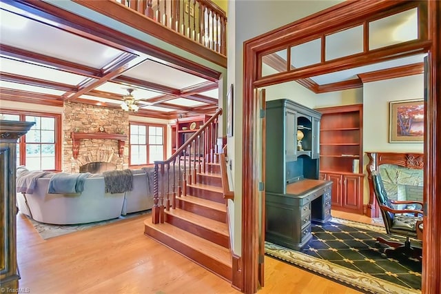 stairs with coffered ceiling, a stone fireplace, a wealth of natural light, and wood-type flooring