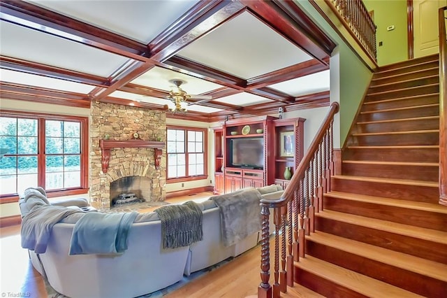 living room featuring light wood-type flooring, beam ceiling, ceiling fan, coffered ceiling, and a stone fireplace