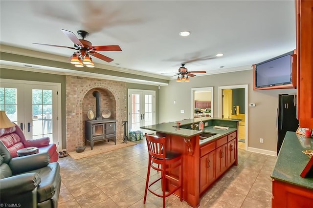 kitchen with french doors, a wood stove, black refrigerator, a kitchen island with sink, and crown molding