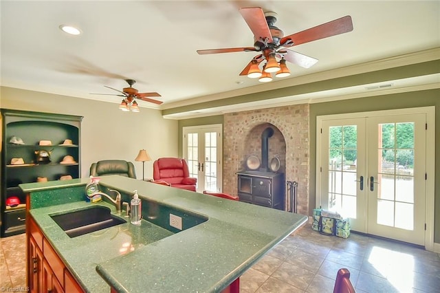 kitchen featuring sink, a wood stove, french doors, a center island with sink, and crown molding