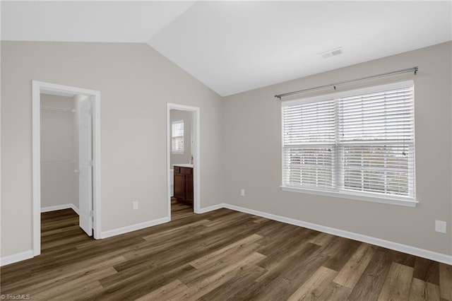 unfurnished bedroom featuring vaulted ceiling, a walk in closet, dark wood-type flooring, and a closet