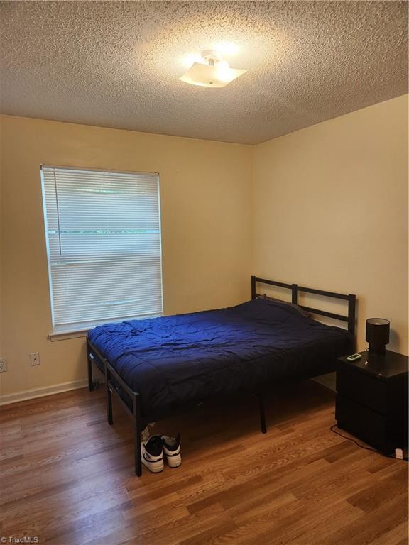 5517 Hornaday Rd Unit D, Greensboro, NC 27409 - bedroom featuring wood finished floors, a textured ceiling, and baseboards