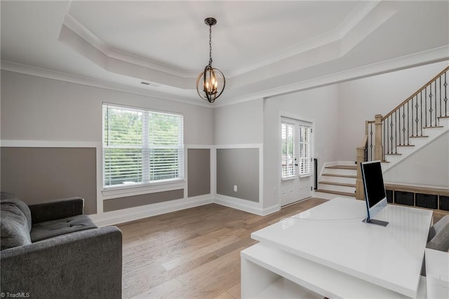 living room with light wood-type flooring, a healthy amount of sunlight, ornamental molding, and a tray ceiling