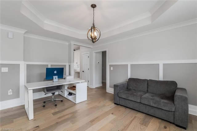 office space with a notable chandelier, light wood-type flooring, a raised ceiling, and ornamental molding