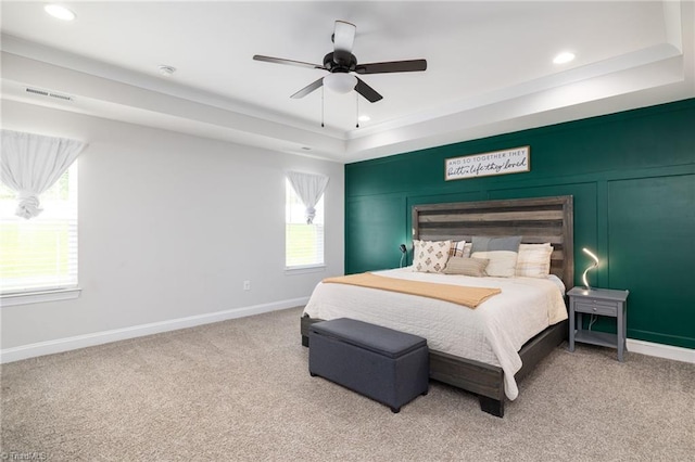 bedroom with light colored carpet, visible vents, multiple windows, and a raised ceiling