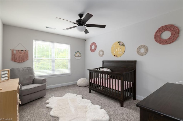 bedroom with a crib, light colored carpet, and ceiling fan