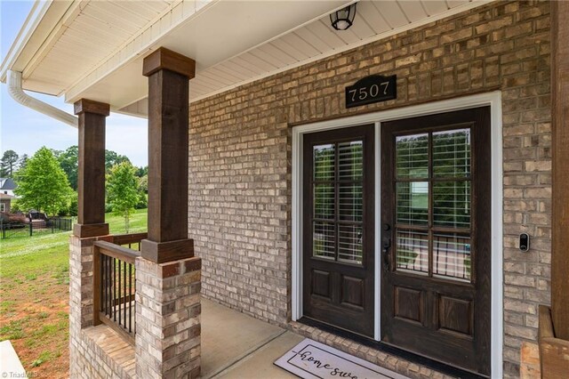 view of exterior entry featuring covered porch and brick siding